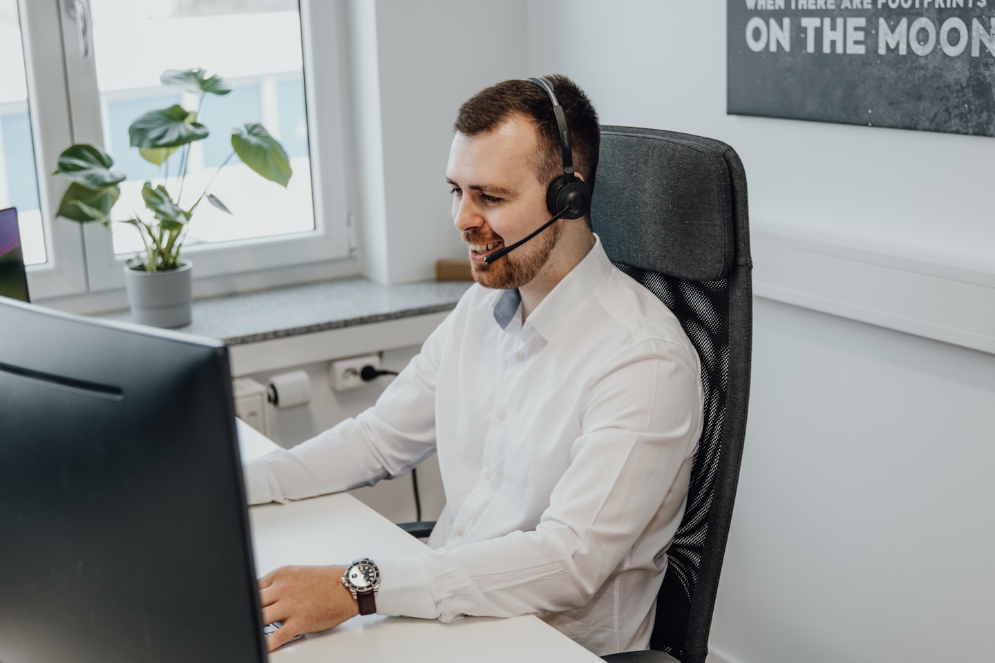 Man in headset smiles while working at a computer.